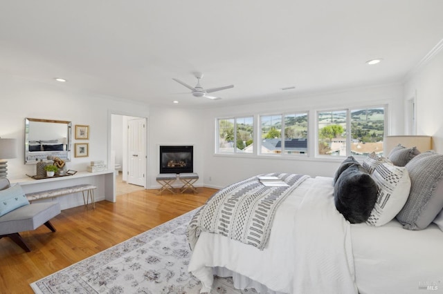 bedroom with a glass covered fireplace, recessed lighting, light wood-type flooring, and ceiling fan