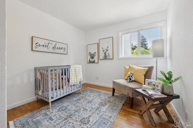 bedroom featuring a crib, baseboards, and hardwood / wood-style floors