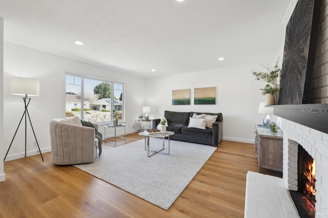 living area with recessed lighting, baseboards, a brick fireplace, and light wood finished floors