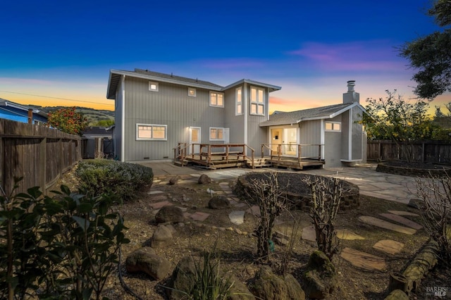 rear view of property featuring a patio area, a deck, a chimney, and a fenced backyard