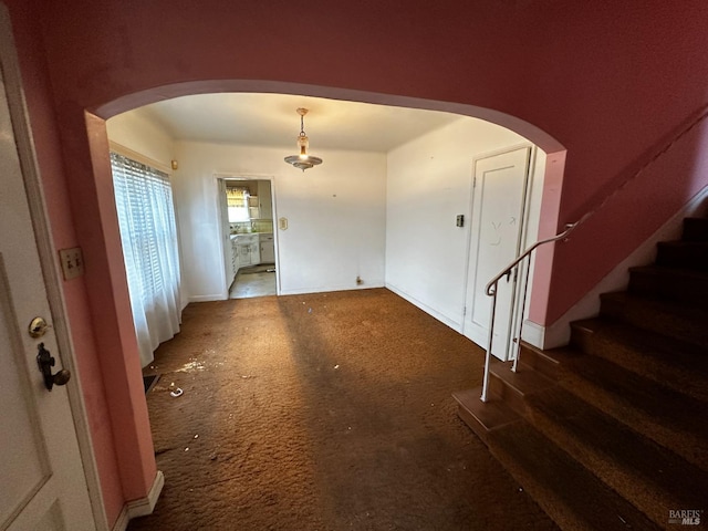 carpeted entryway featuring stairway, baseboards, and arched walkways