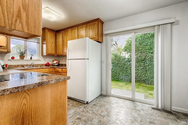 kitchen with dark countertops, visible vents, brown cabinets, and freestanding refrigerator