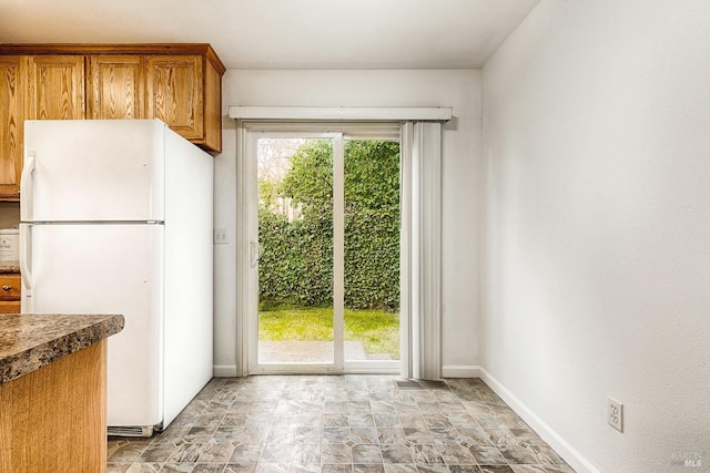 kitchen featuring plenty of natural light, brown cabinets, stone finish flooring, and freestanding refrigerator