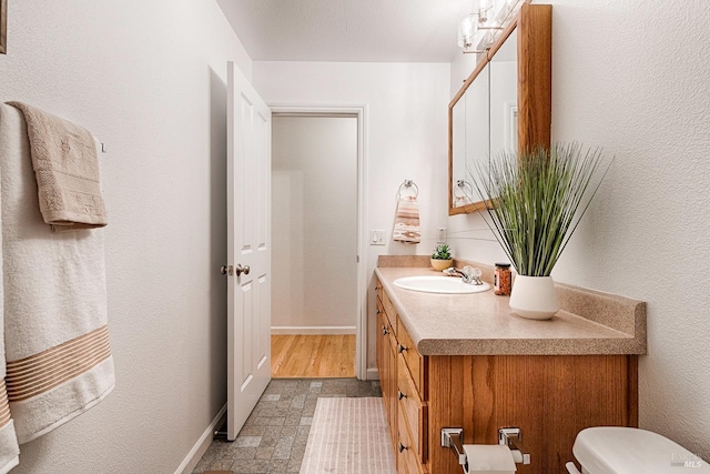 half bathroom with vanity, stone finish floor, toilet, and baseboards