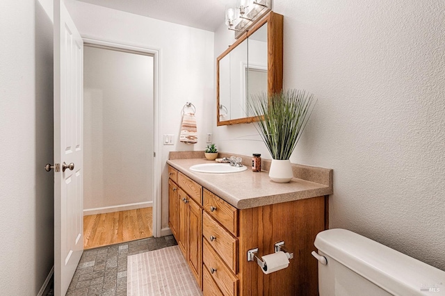 bathroom featuring baseboards, toilet, vanity, and a textured wall