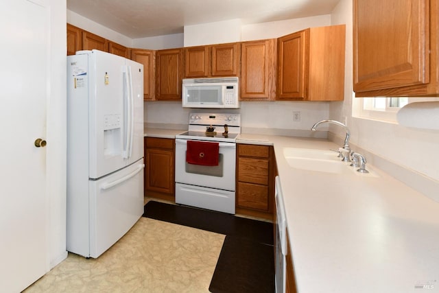 kitchen with brown cabinetry, white appliances, light countertops, and a sink