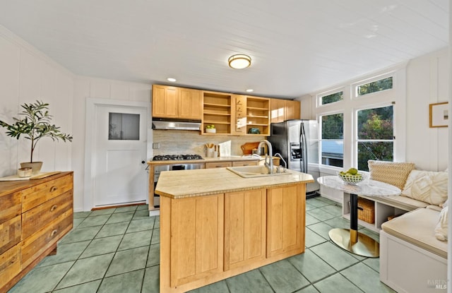 kitchen with under cabinet range hood, a center island with sink, light countertops, stainless steel appliances, and a sink