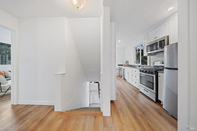 kitchen featuring white cabinets, appliances with stainless steel finishes, light wood-type flooring, and a sink