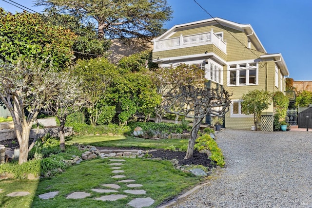 shingle-style home with a front lawn, gravel driveway, and a balcony