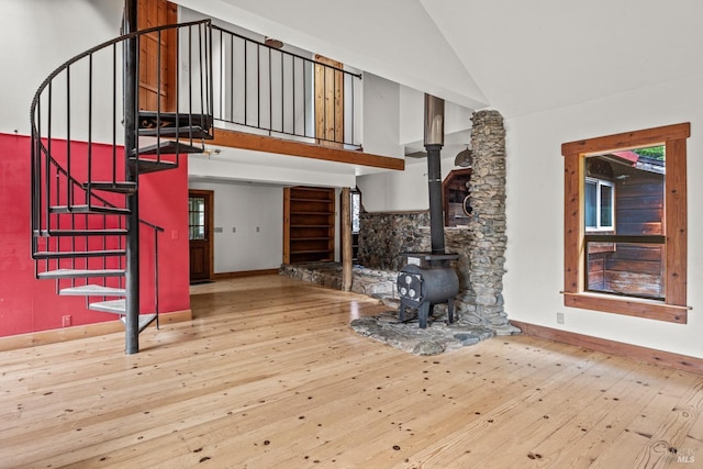 living room featuring baseboards, high vaulted ceiling, a wood stove, stairs, and hardwood / wood-style flooring