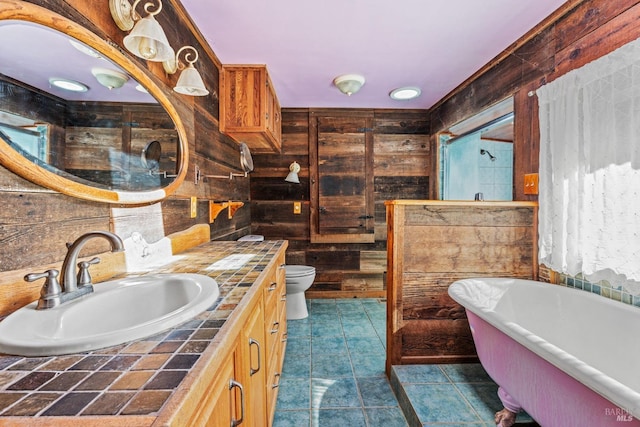 full bath featuring tile patterned flooring, wood walls, toilet, a freestanding tub, and vanity