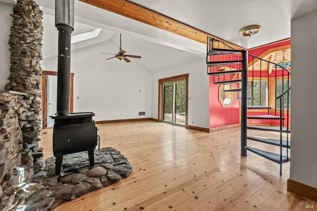 living room with baseboards, stairs, beam ceiling, a wood stove, and hardwood / wood-style flooring