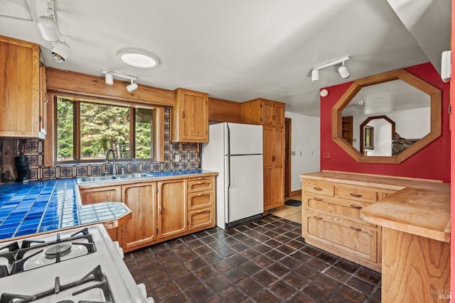 kitchen with white appliances, tile countertops, a sink, tasteful backsplash, and brown cabinets