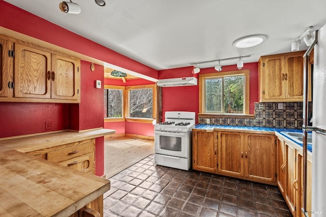 kitchen featuring under cabinet range hood, decorative backsplash, brown cabinets, and white range with gas stovetop