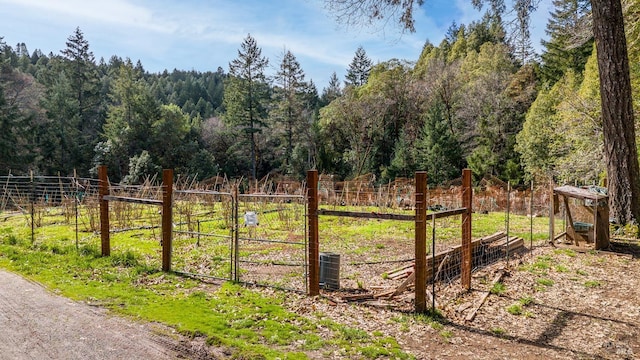 view of yard with a gate, fence, a forest view, and central AC