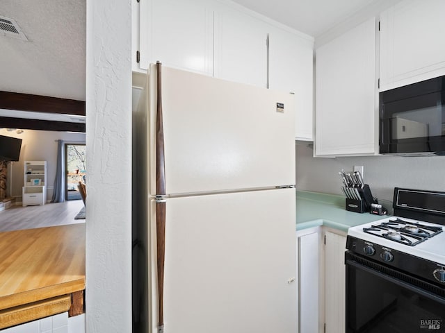 kitchen with freestanding refrigerator, white cabinets, black microwave, light countertops, and gas range