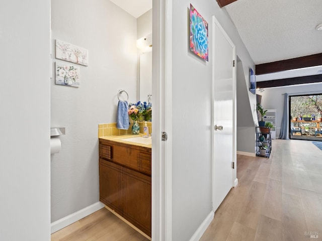 interior space with beamed ceiling, vanity, baseboards, and wood finished floors