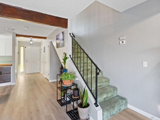 stairs with visible vents, beamed ceiling, a textured ceiling, wood finished floors, and baseboards