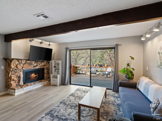 living room featuring light wood finished floors, visible vents, beamed ceiling, a fireplace, and a textured ceiling