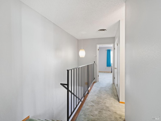 hall featuring baseboards, carpet, visible vents, and a textured ceiling