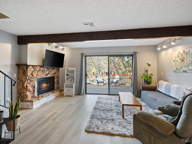 living area with visible vents, beam ceiling, a stone fireplace, and wood finished floors