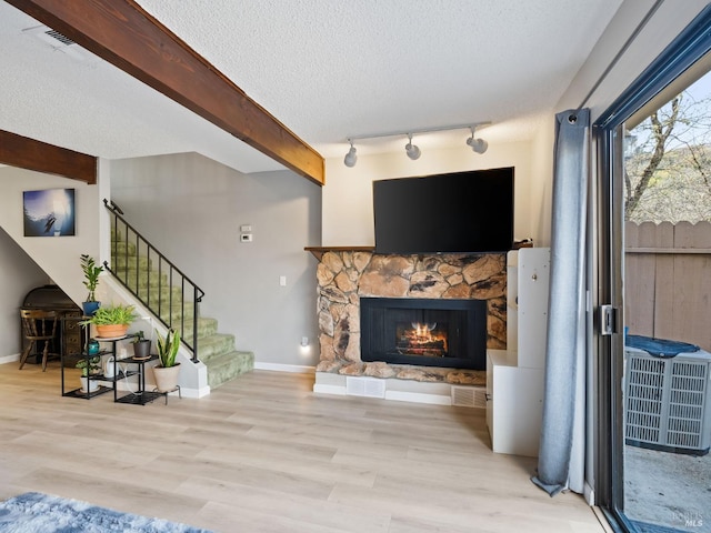 living room featuring stairway, wood finished floors, a stone fireplace, a textured ceiling, and beamed ceiling