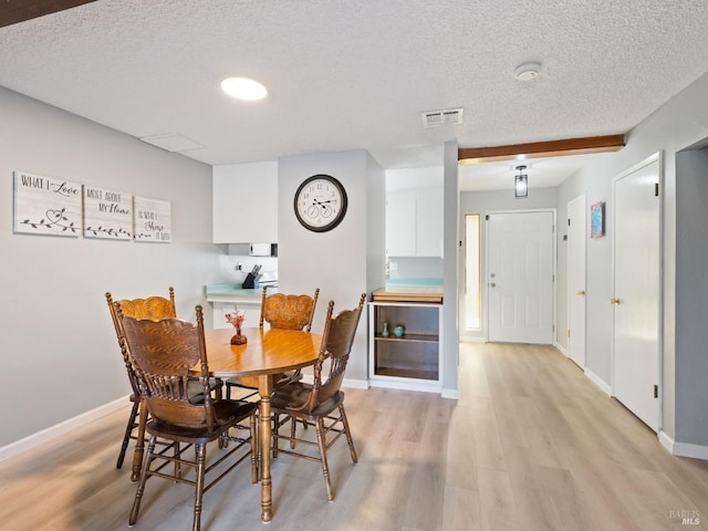 dining room featuring visible vents, light wood-style flooring, a textured ceiling, and baseboards