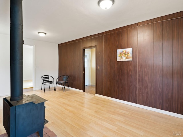 sitting room with wooden walls, baseboards, light wood-style floors, and a wood stove