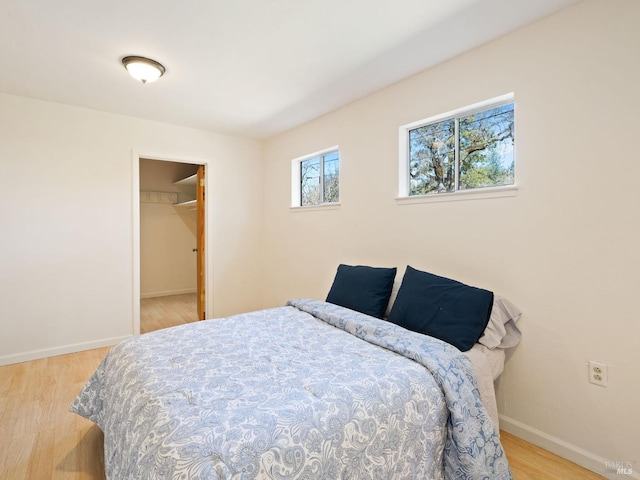 bedroom with a walk in closet, baseboards, and wood finished floors