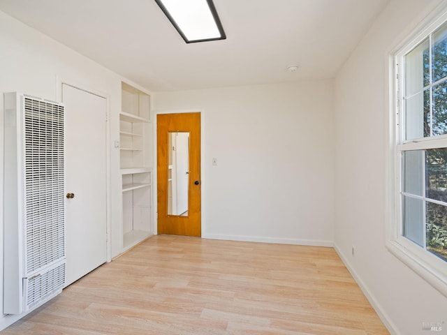 unfurnished room featuring built in features, wood finished floors, a heating unit, and baseboards