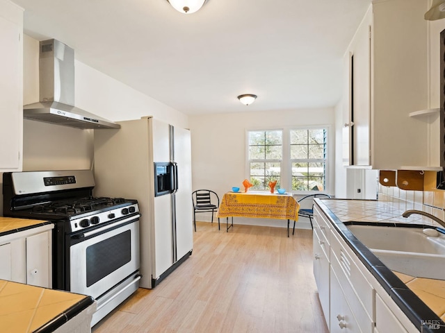 kitchen with a sink, stainless steel gas range, wall chimney range hood, and tile counters