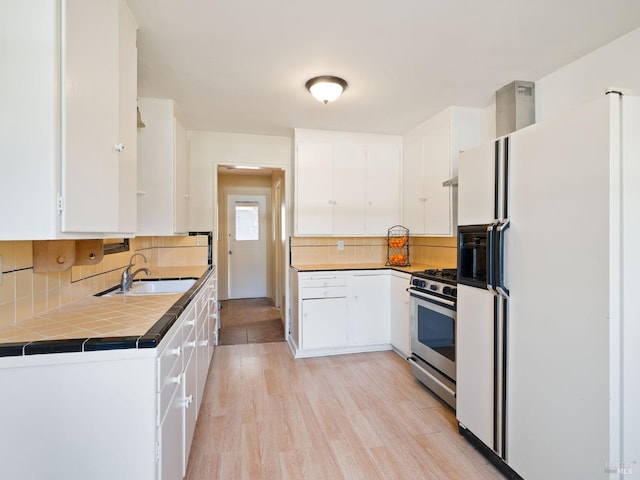 kitchen featuring white cabinets, stainless steel gas stove, white fridge with ice dispenser, and a sink