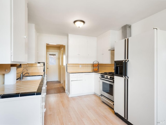 kitchen featuring stainless steel gas range, decorative backsplash, white refrigerator with ice dispenser, white cabinetry, and a sink