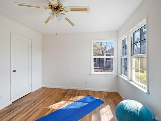 exercise area featuring baseboards, wood finished floors, and a ceiling fan