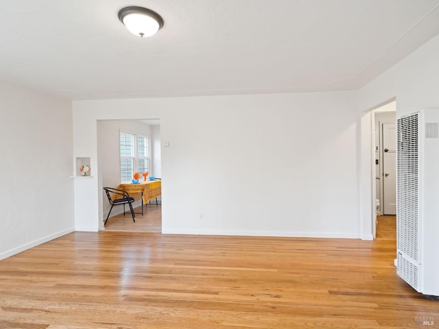 empty room with light wood-style flooring, baseboards, and a heating unit