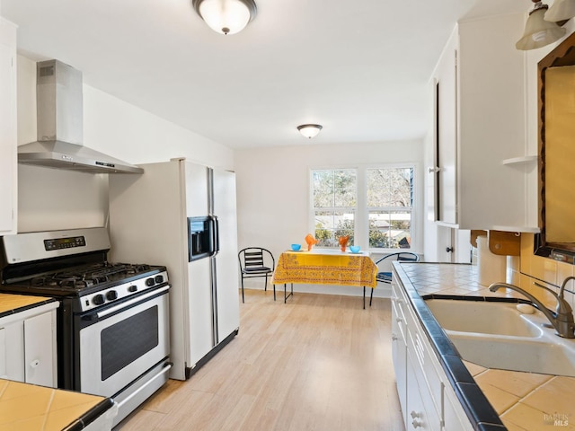 kitchen featuring tile counters, wall chimney range hood, stainless steel range with gas stovetop, and a sink