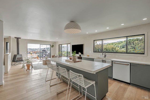 kitchen featuring a breakfast bar, gray cabinets, white dishwasher, light countertops, and a wood stove