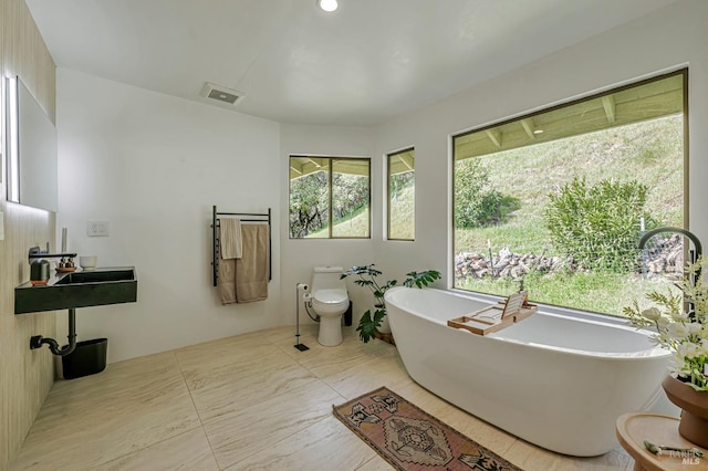 full bath with a freestanding tub, marble finish floor, visible vents, and toilet