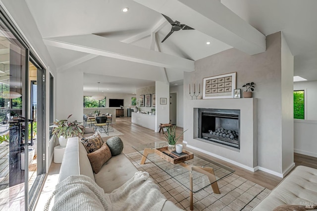 living area featuring a glass covered fireplace, vaulted ceiling with beams, light wood-type flooring, and ceiling fan