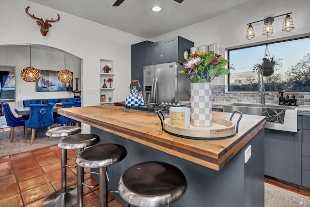 kitchen with a ceiling fan, tasteful backsplash, stainless steel fridge, a breakfast bar area, and butcher block counters