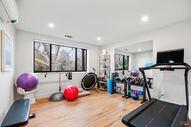 exercise area with a wall mounted air conditioner, visible vents, wood finished floors, recessed lighting, and baseboards