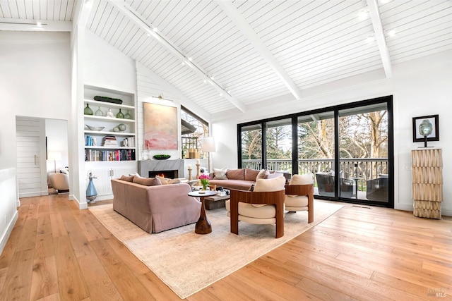 living room featuring hardwood / wood-style floors, high vaulted ceiling, a premium fireplace, beam ceiling, and track lighting