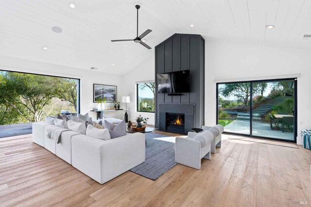 living area with a large fireplace, vaulted ceiling, and light wood finished floors