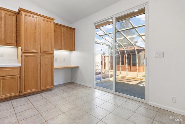 unfurnished dining area with baseboards, light tile patterned flooring, built in desk, and vaulted ceiling