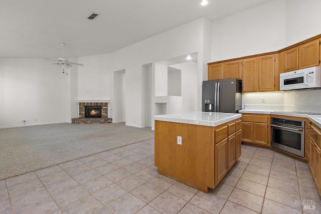 kitchen with light carpet, tile countertops, stainless steel oven, white microwave, and black refrigerator with ice dispenser