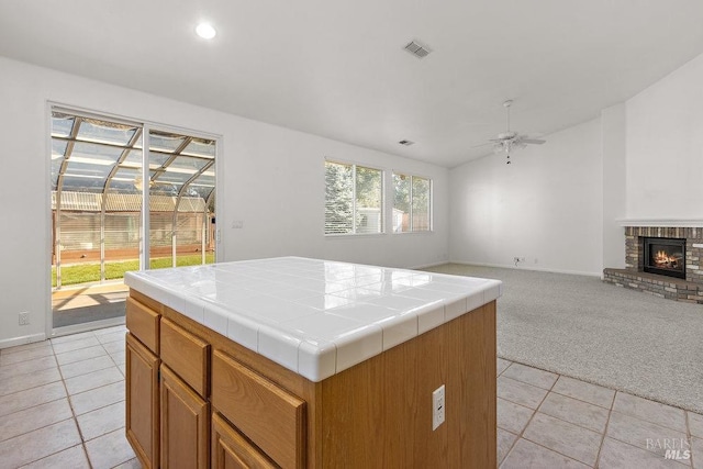 kitchen with light carpet, open floor plan, a fireplace, tile counters, and ceiling fan