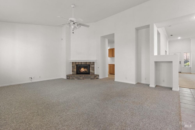 unfurnished living room featuring a brick fireplace, light colored carpet, a towering ceiling, and ceiling fan