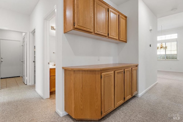 hallway featuring a notable chandelier, light colored carpet, and baseboards