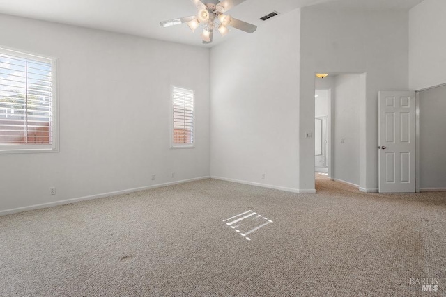 carpeted spare room featuring a high ceiling, visible vents, baseboards, and ceiling fan