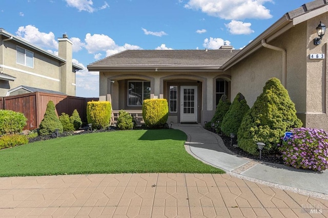 doorway to property featuring fence, a lawn, and stucco siding